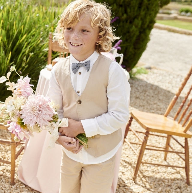 Junge in sommerlicher Festmode für Kinder und einem Blumenstrauß in der Hand