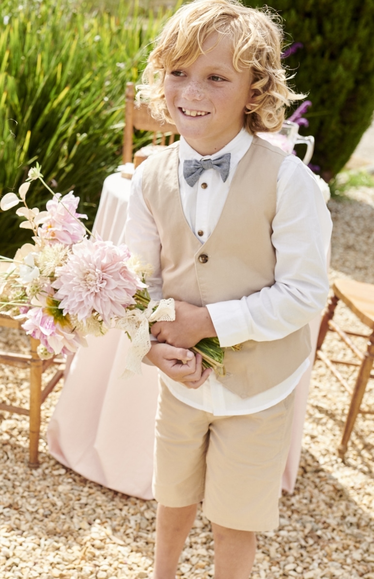 Junge in sommerlicher Festmode für Kinder und einem Blumenstrauß in der Hand