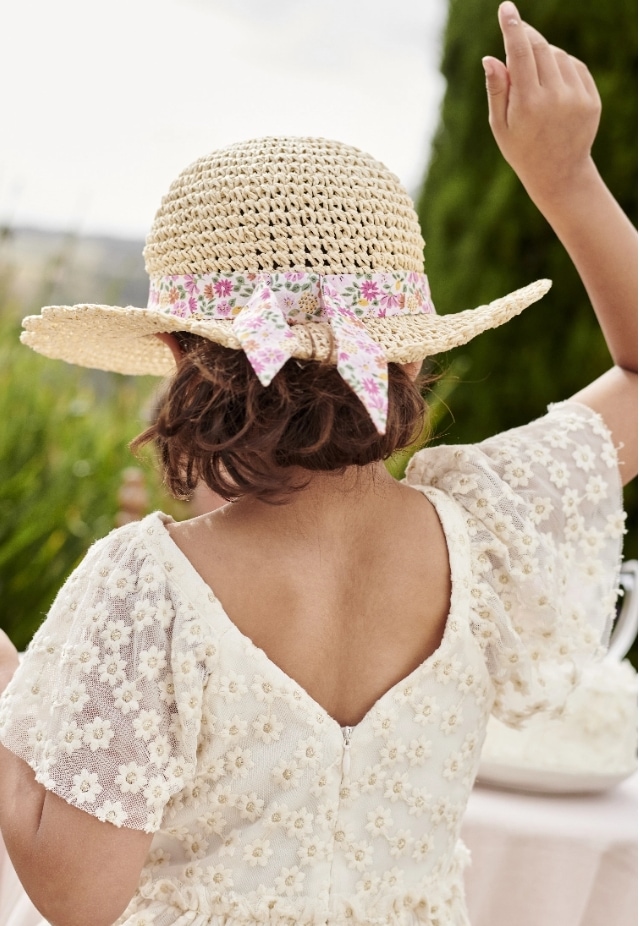 Mädchen von hinten in einem weißen Kleid und festlichem Hut