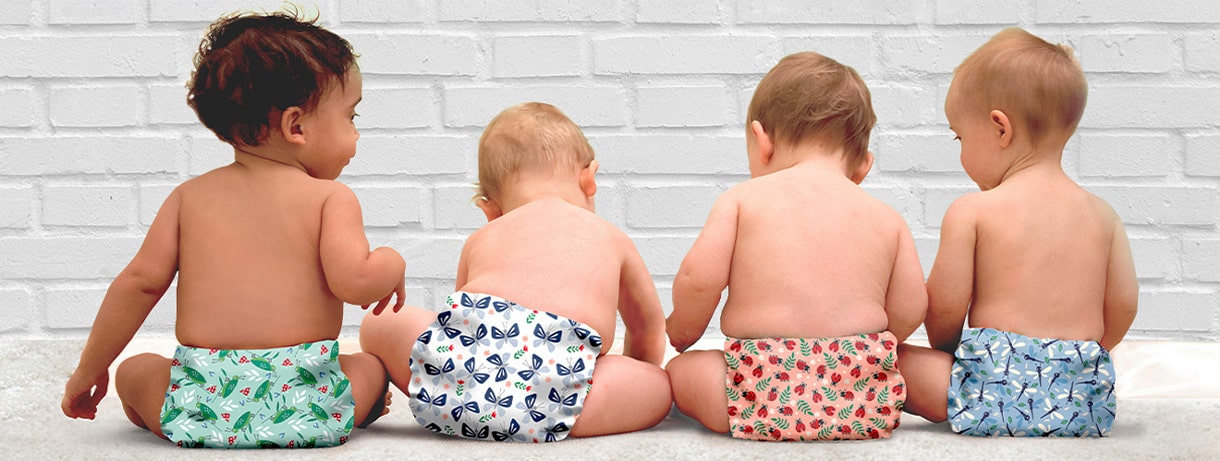 Babys in Stoffwindeln von vertbaudet mit bunten Motiven sitzen nebeneinander